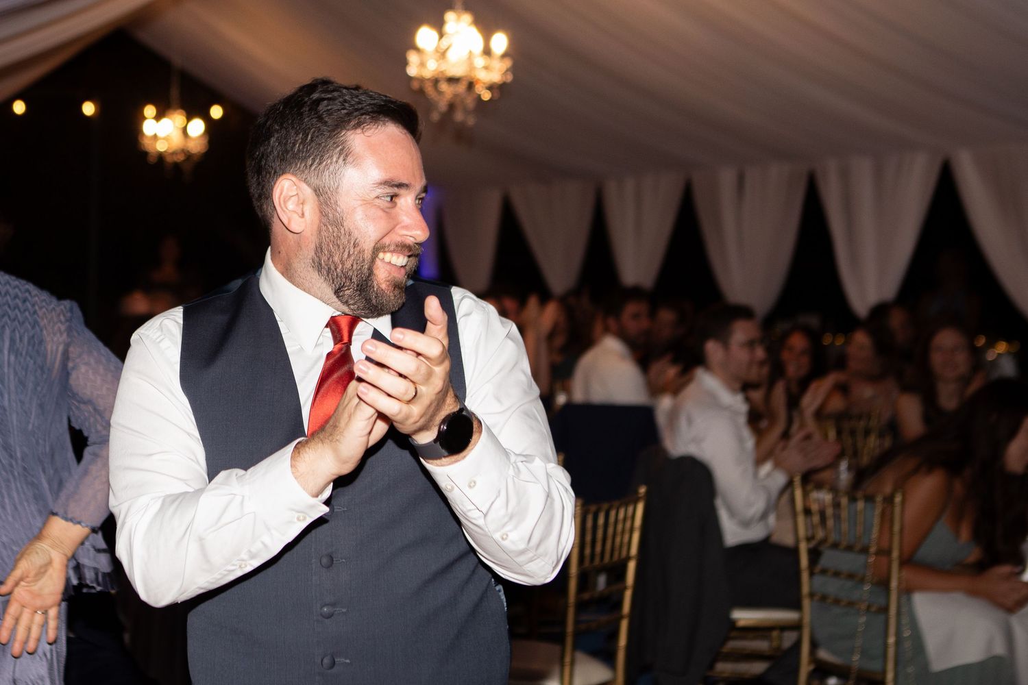 A person in formal attire laughs enthusiastically during a reception in an elegantly decorated tent venue.