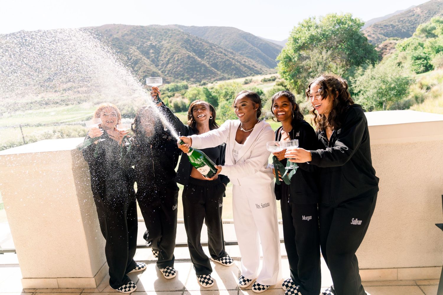 Wedding party celebrating with champagne on balcony with mountain views.