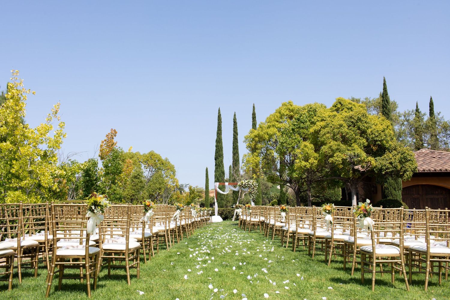 Garden wedding venue with rows of wooden chairs and flower petals along a grassy aisle.