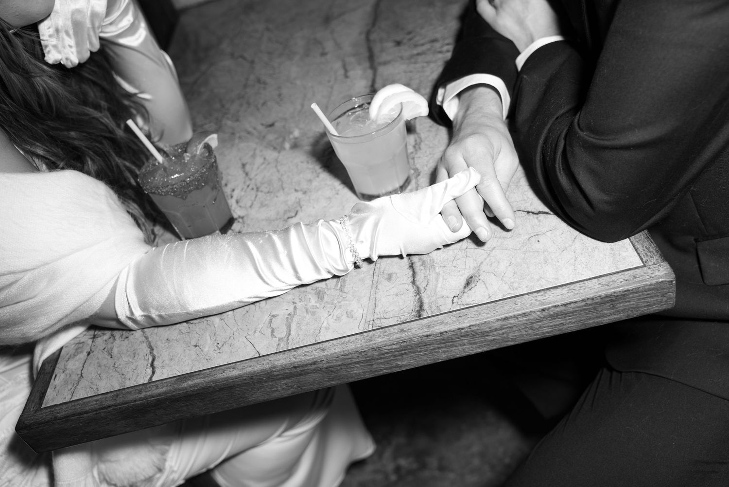 Black and white closeup of hands signing or writing on a document at a wooden table.