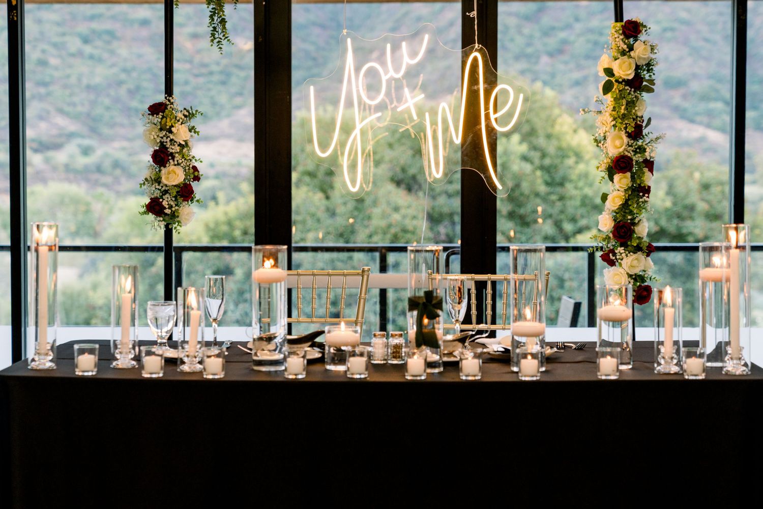 Modern wedding reception table with You & Me neon sign against mountain backdrop.