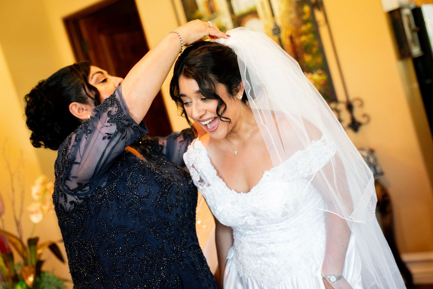 A joyful candid moment between a bride in white dress and veil dancing with a guest in blue at a wedding reception.