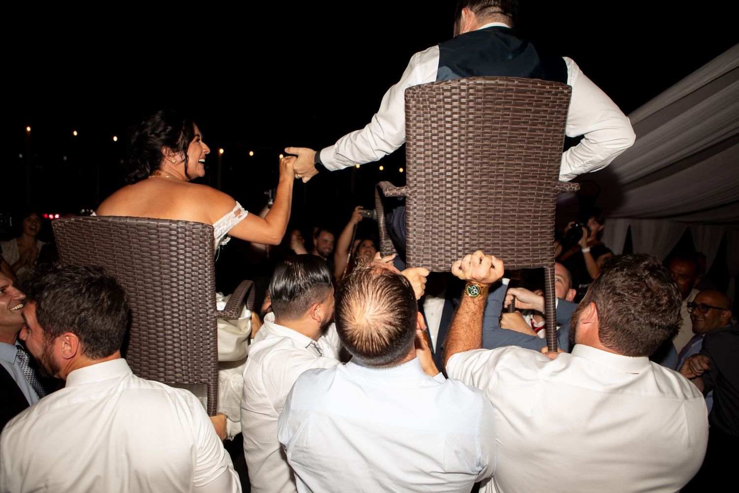 Wedding guests celebrate by lifting people on chairs during an energetic reception dance party.