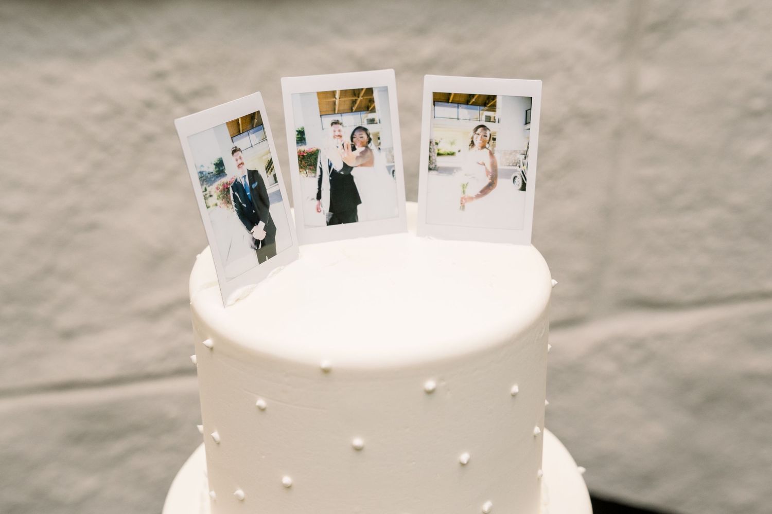White wedding cake decorated with polaroid photos as toppers.