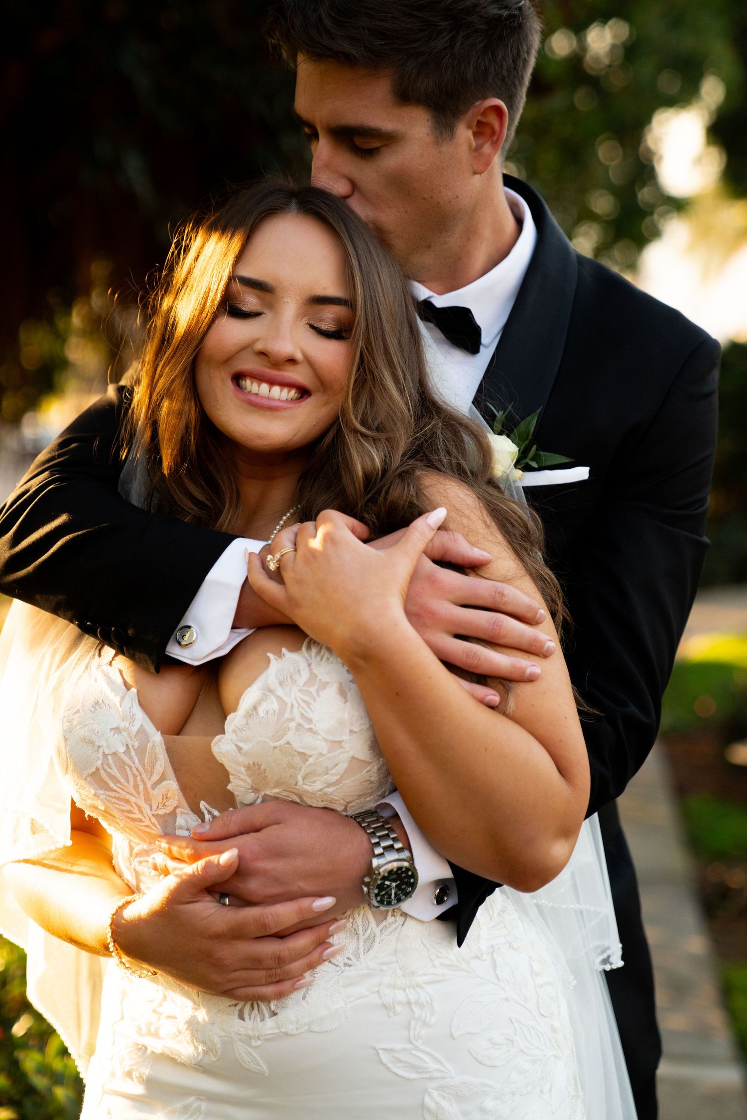 Romantic wedding portrait of a couple embracing in golden sunlight with bride wearing a lace white dress.