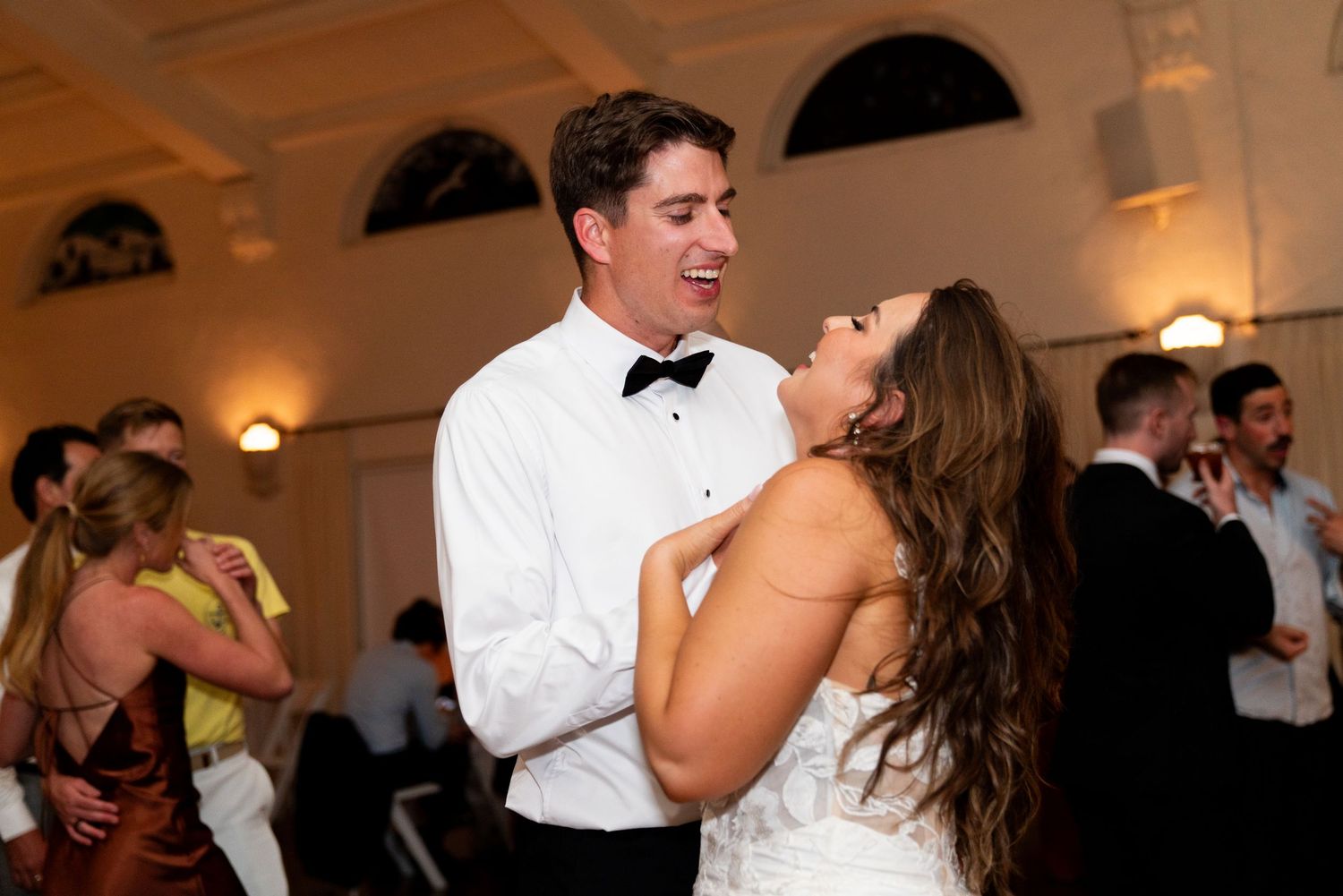 A couple shares a playful moment while dancing at their wedding reception in an elegant ballroom.