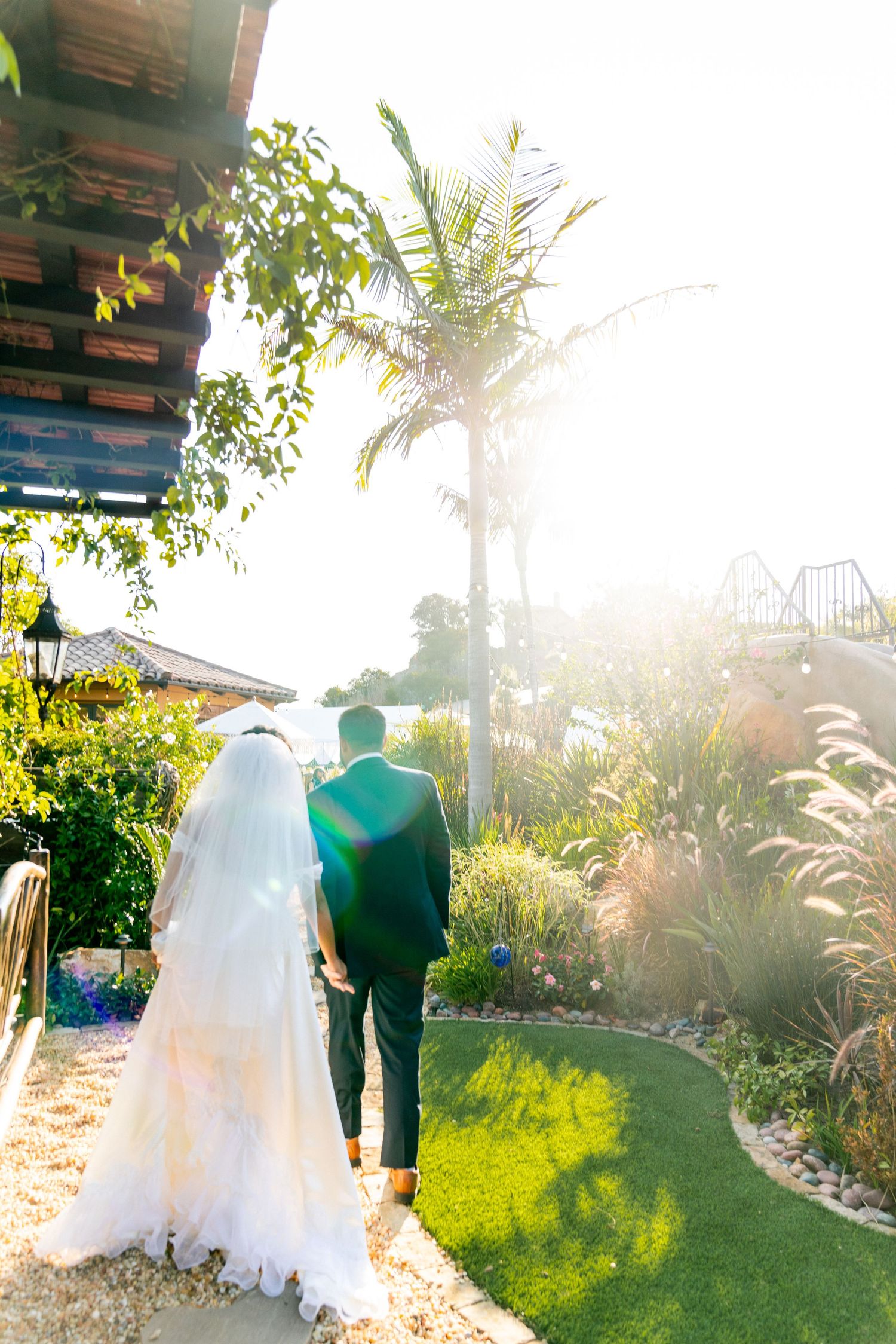 A romantic sunset wedding photo of a couple walking through a tropical paradise garden path.
