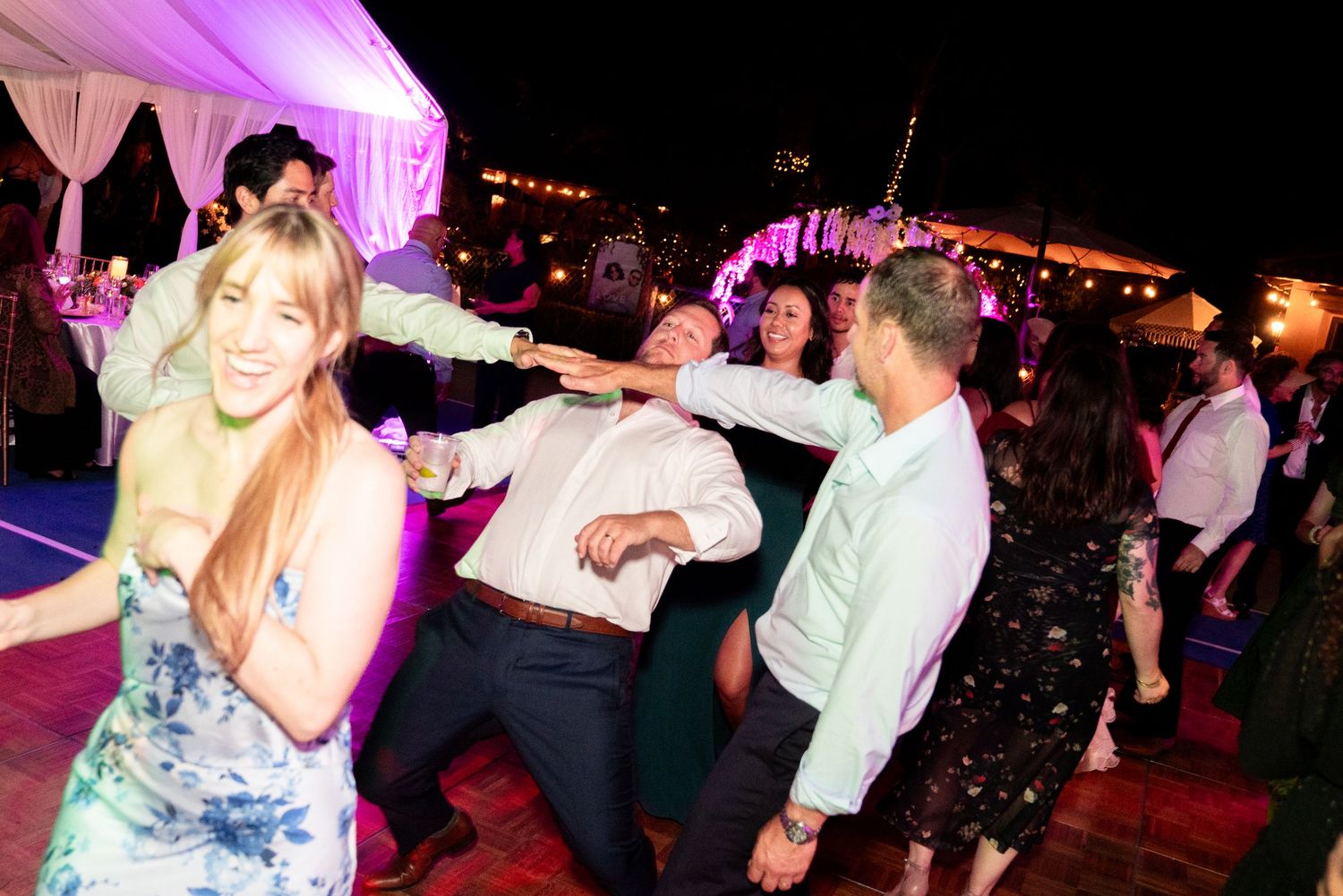 Night wedding reception with guests dancing under colorful lights and white tent.