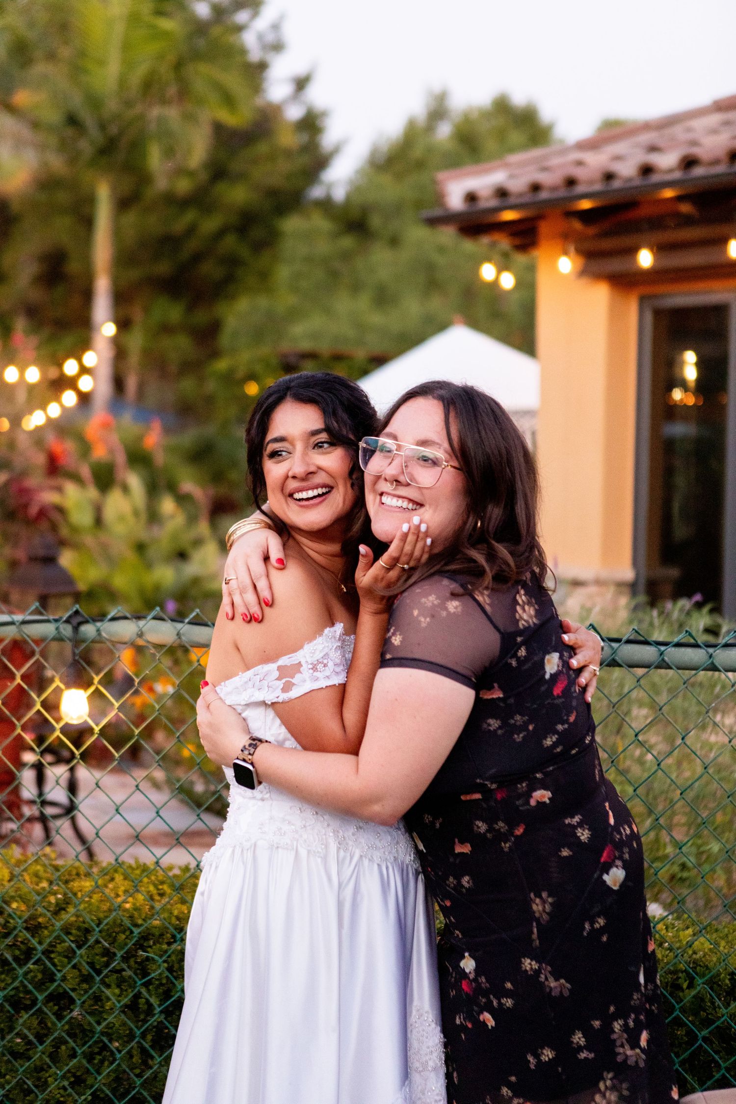 Outdoor wedding celebration with string lights and terracotta-colored Mediterranean architecture.