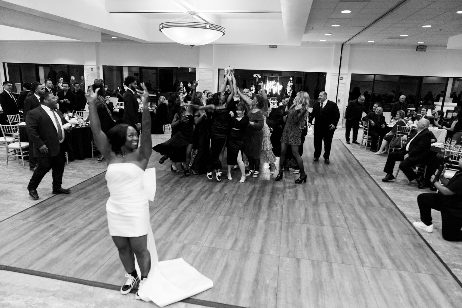 Black and white photo of wedding guests dancing in a circle on the reception dance floor.