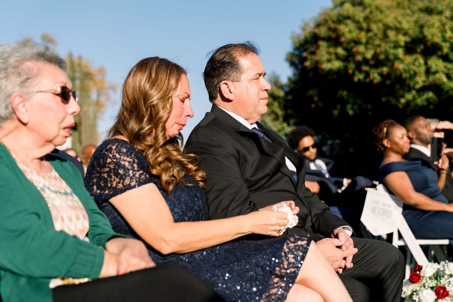 Wedding guests watching the ceremony from white chairs outdoors.