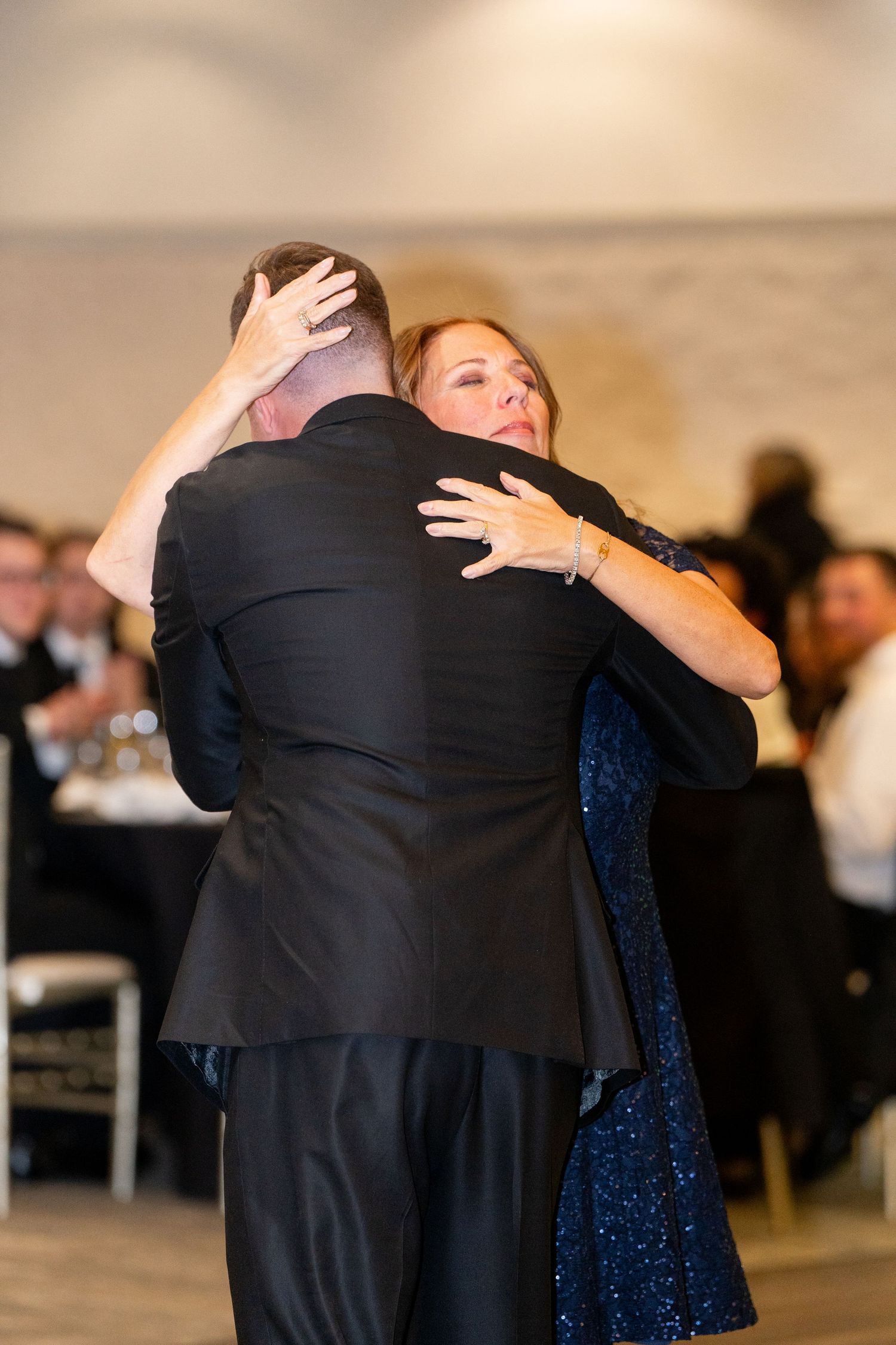 A couple embraces during a dance at a formal event, with the woman wearing a sparkling blue dress.