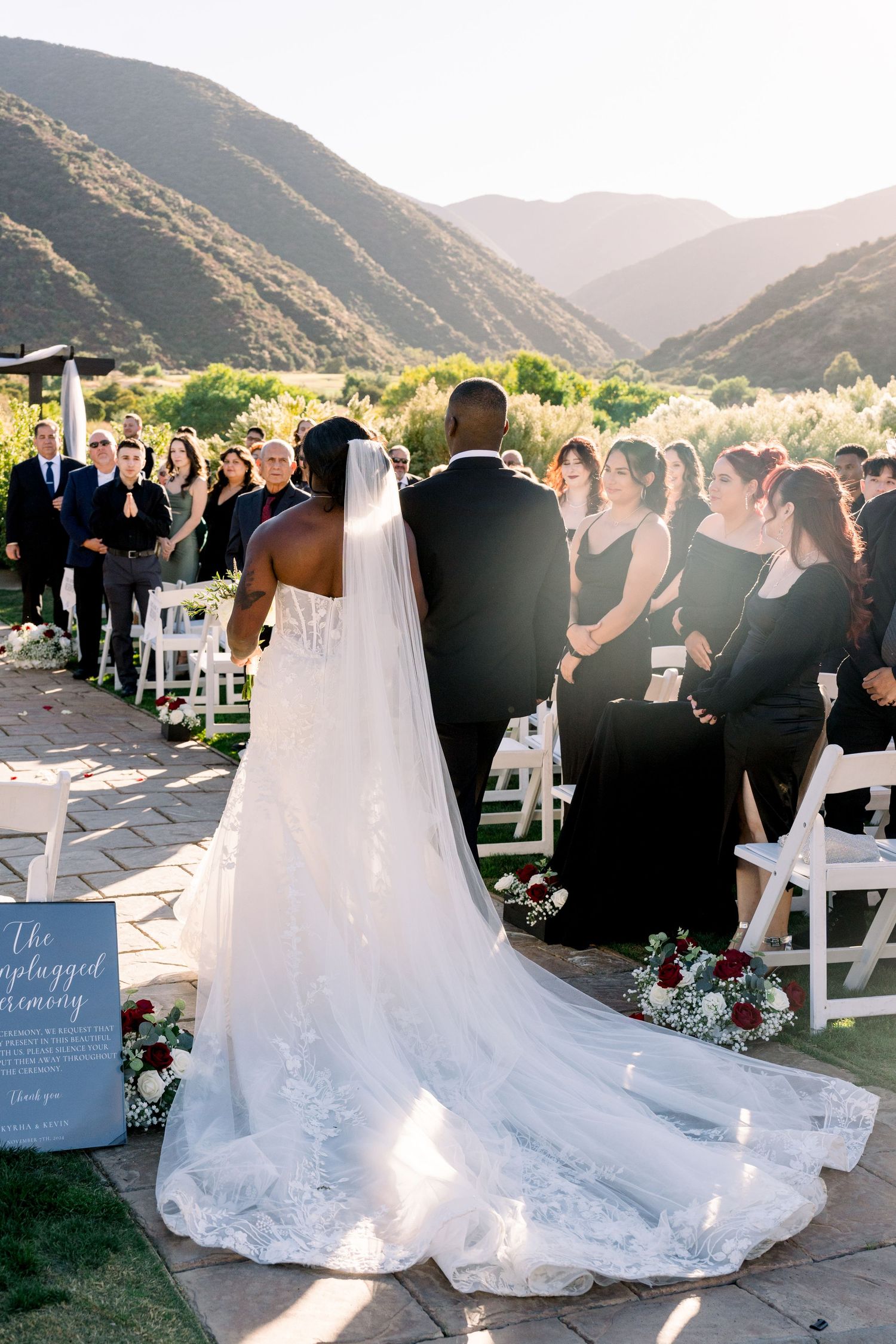 A wedding ceremony taking place outdoors with a scenic mountain backdrop and flowing white wedding dress.