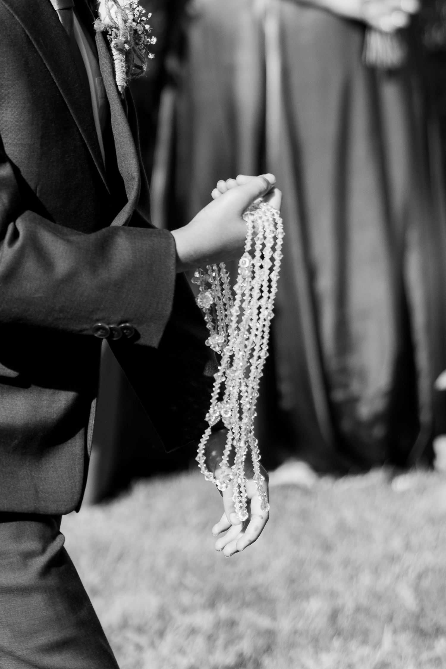 Black and white photo of hands holding delicate pearl strands at a formal event.