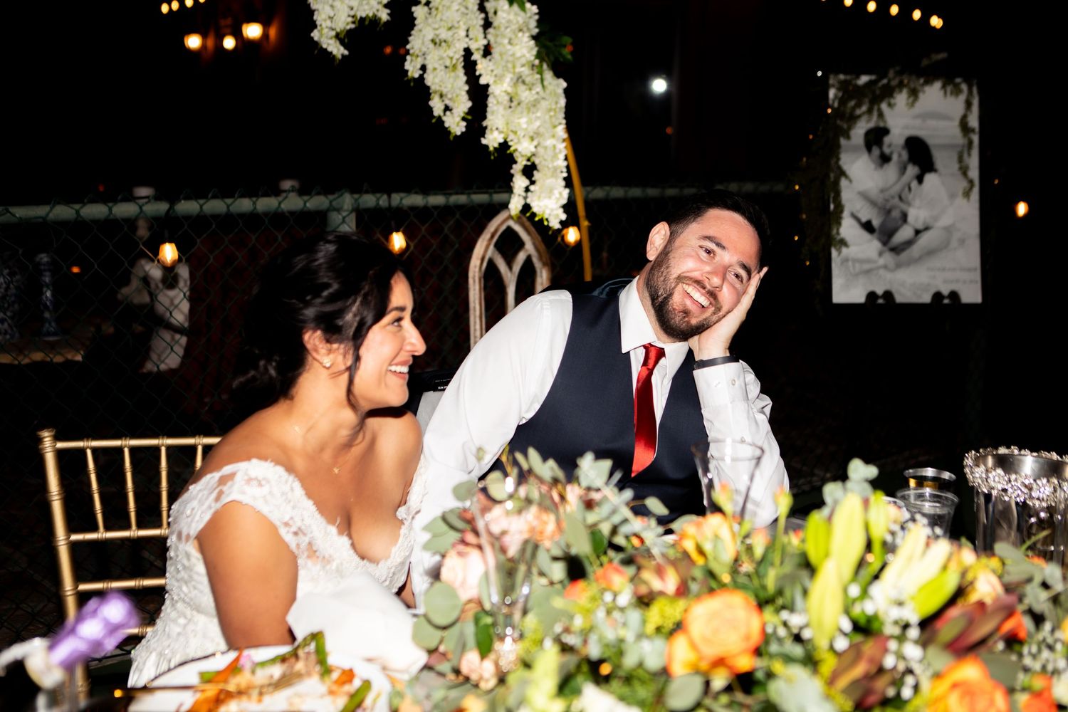 Candid moment of newlyweds laughing together at their reception dinner table.
