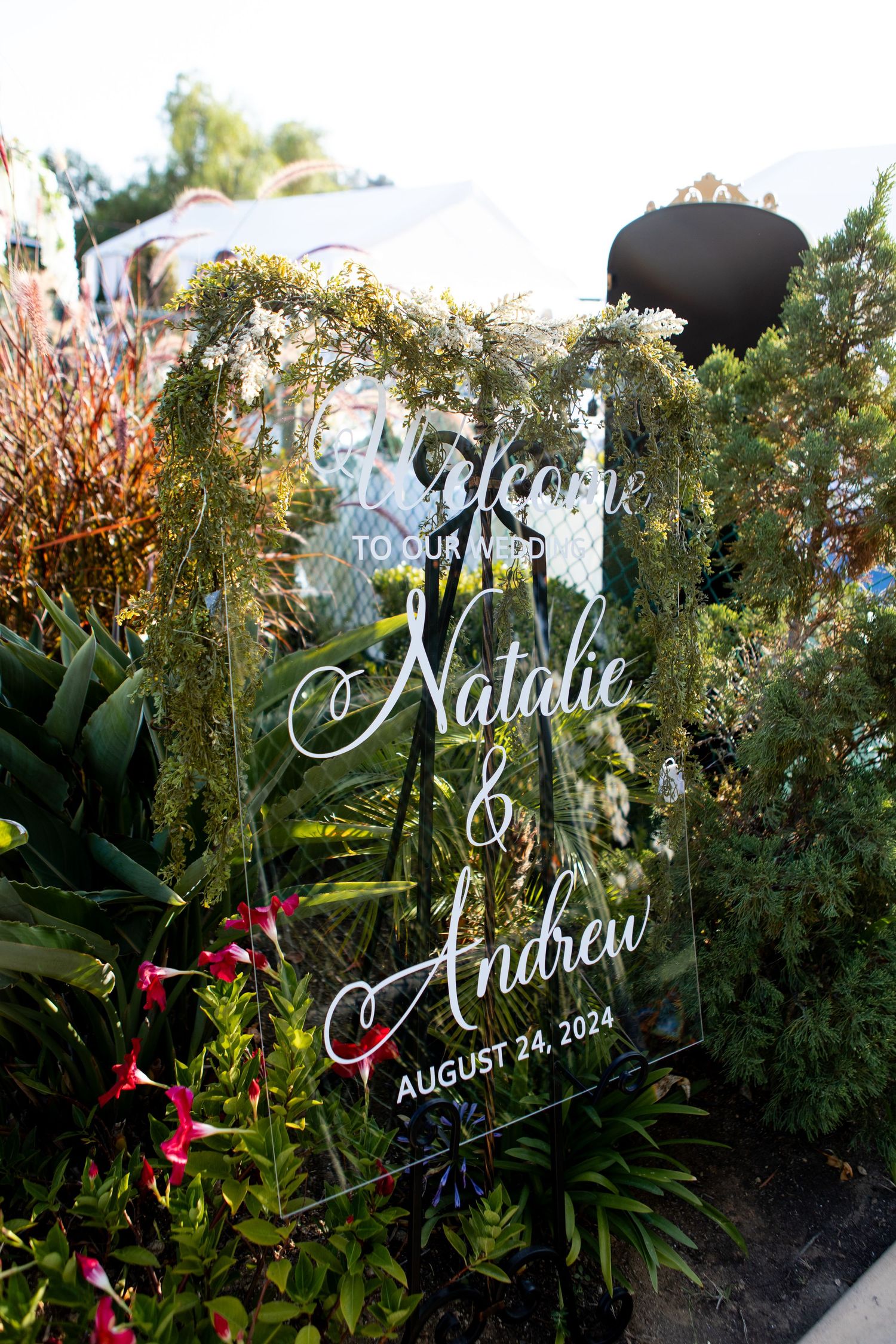 Clear acrylic wedding welcome sign with floral decorations displaying wedding date and names.