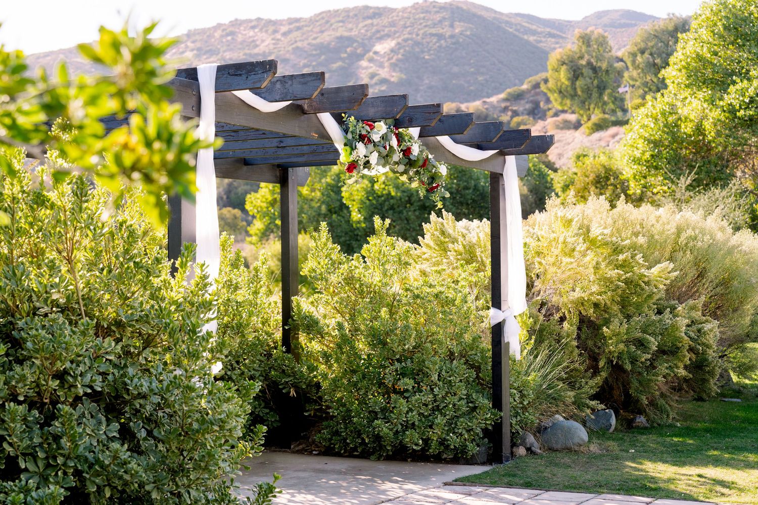White fabric-draped wooden posts create an elegant pathway through lush garden with mountains in background.