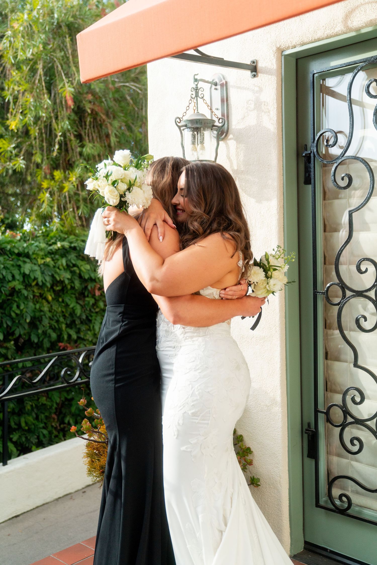 Two people share an emotional embrace during a wedding ceremony, with one wearing a white gown and the other in black.