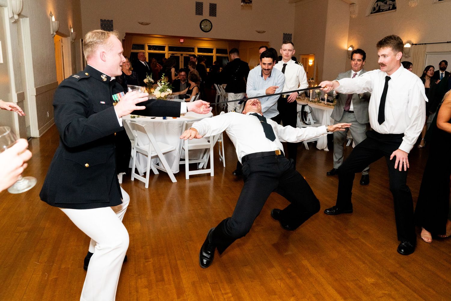 Wedding guests dancing and having fun with limbo dance moves at a reception party on a wooden dance floor.