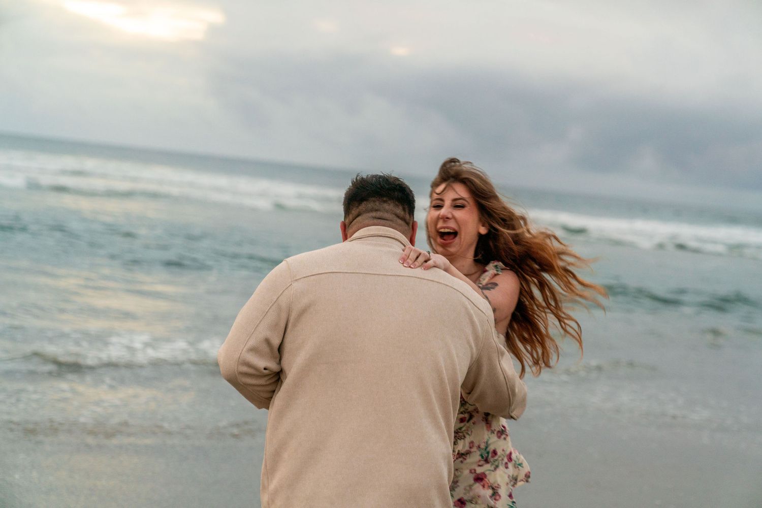 A joyful couple shares a romantic moment together at the beach during sunset as waves crash behind them.