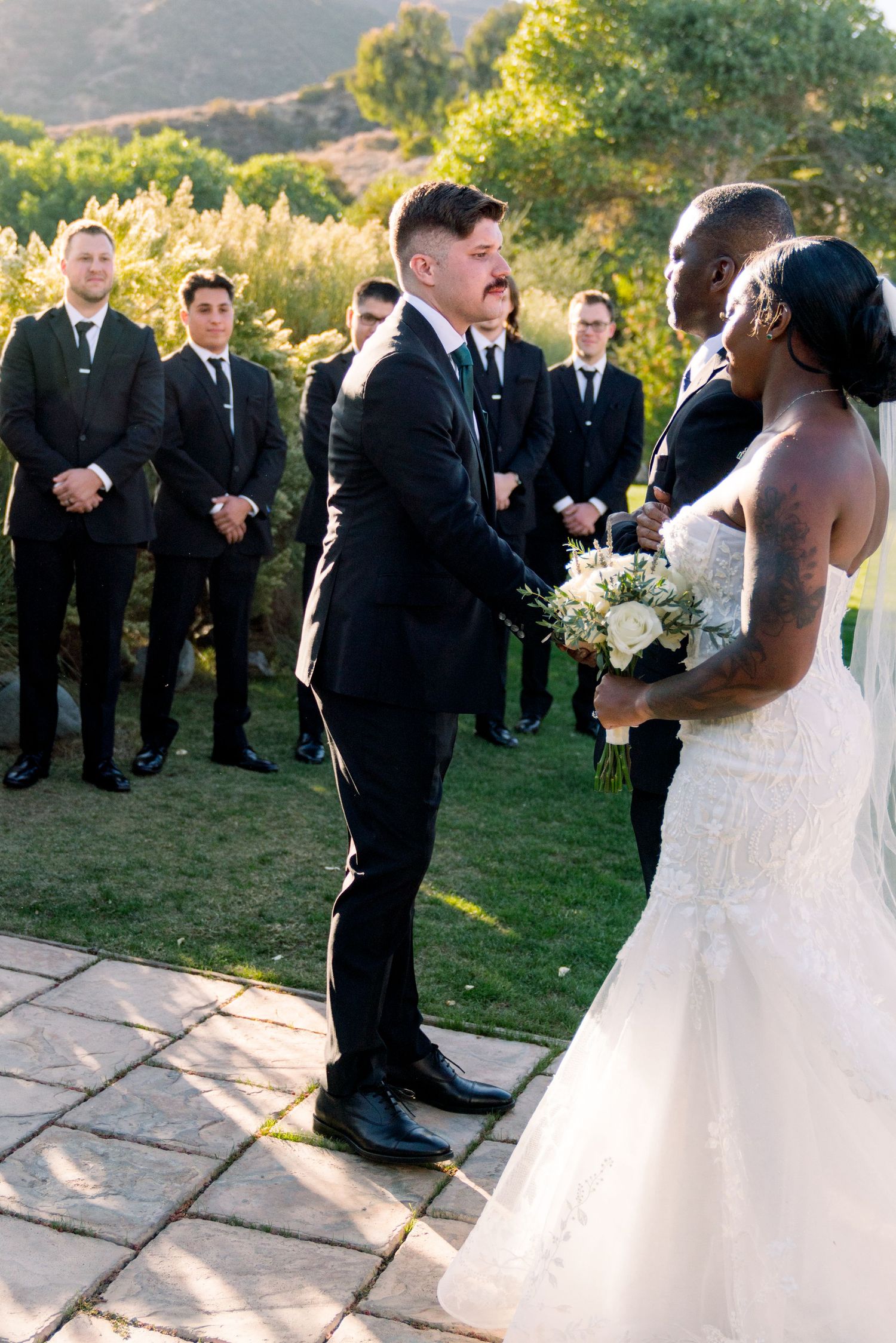 A wedding ceremony takes place on a scenic lawn with mountains in the background.