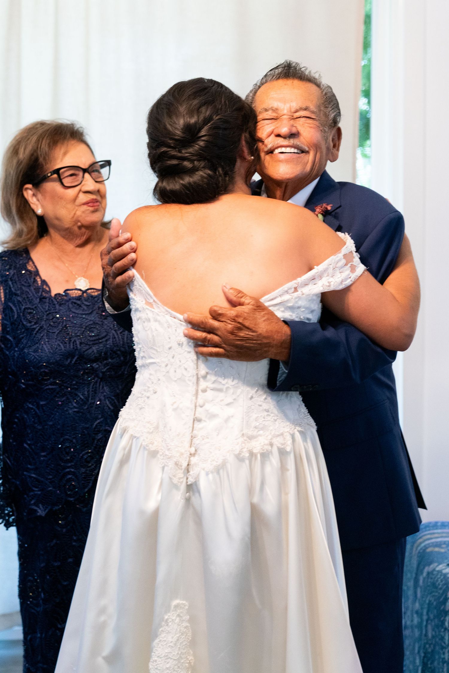 Emotional wedding moment as parents embrace their daughter in her beautiful white bridal gown.