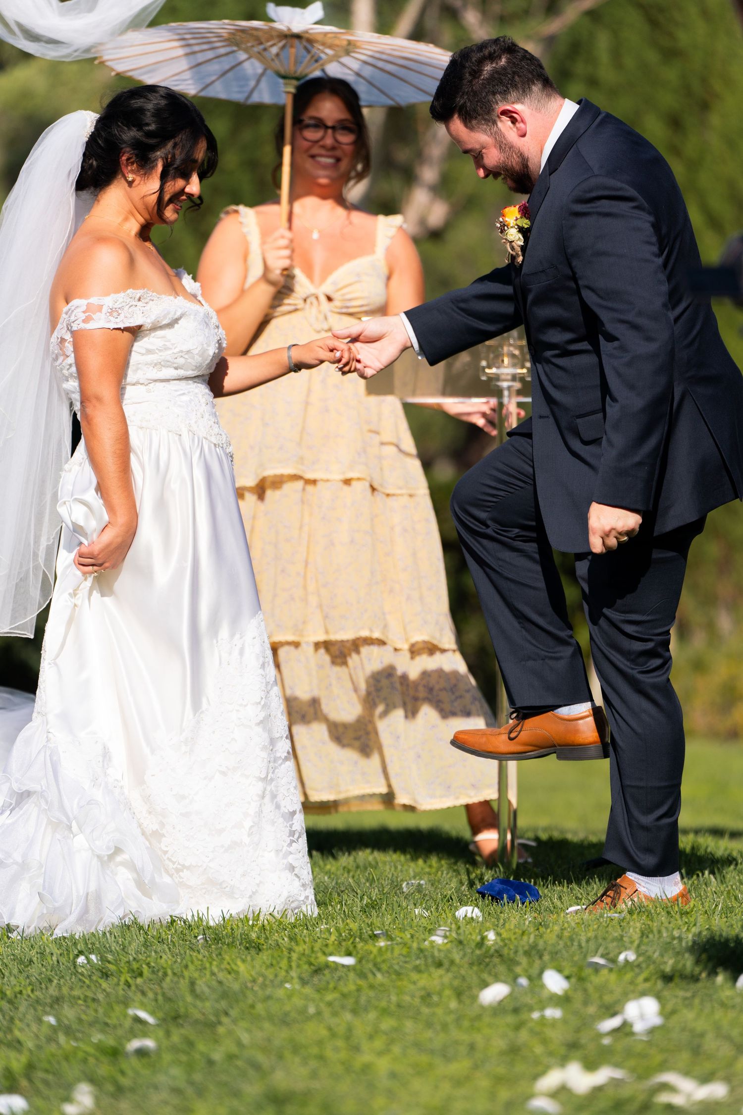 Wedding ceremony moment shows newlyweds and officiant under parasol during outdoor garden celebration.
