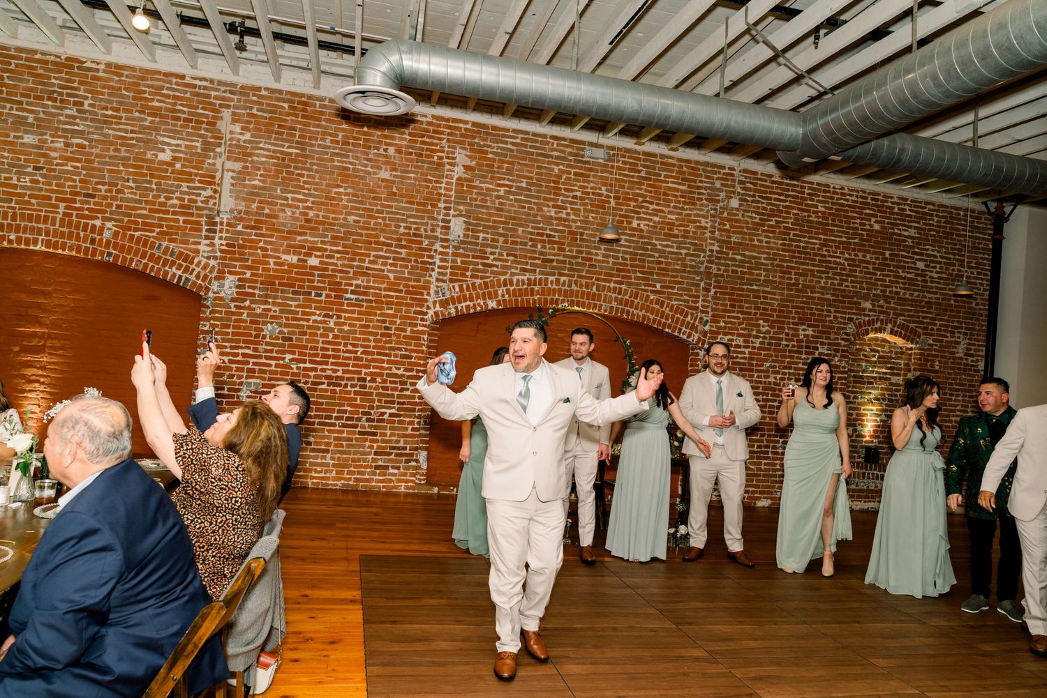 Wedding party celebrating on dance floor with exposed brick walls and industrial ceiling in reception venue.
