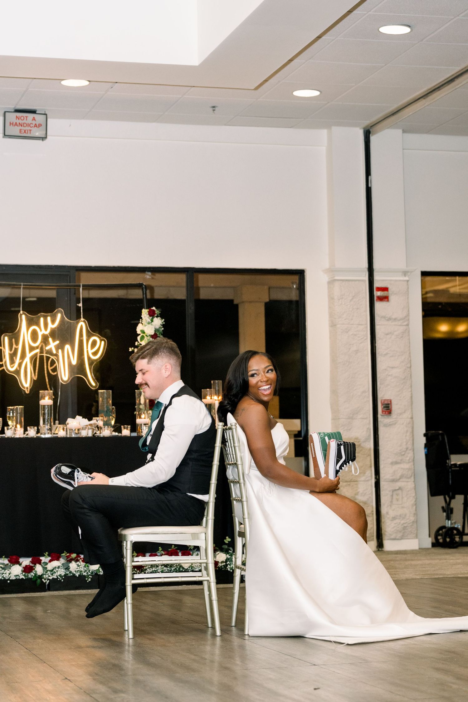 A couple participates in a wedding reception game while seated in decorative chairs.