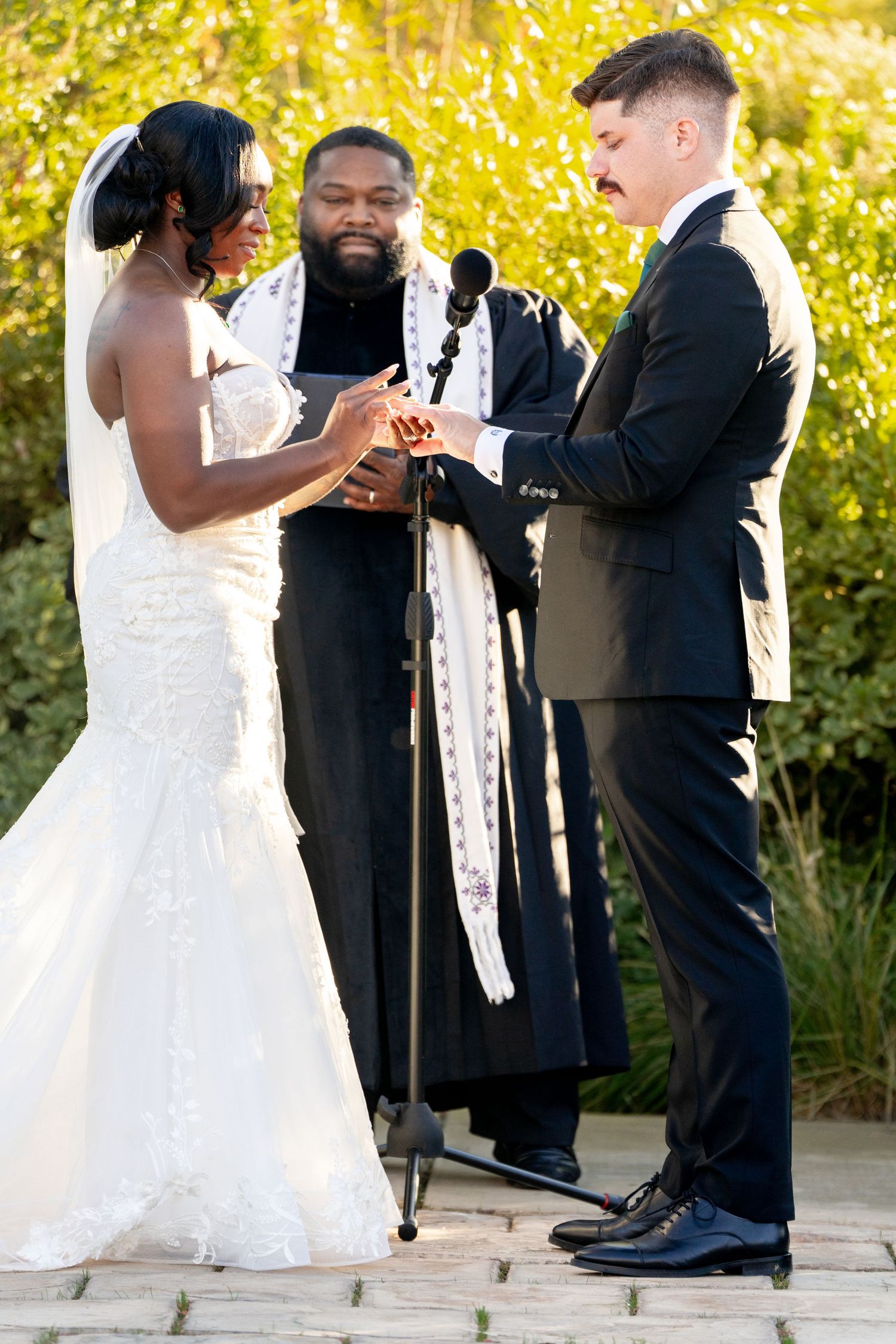An outdoor wedding ceremony with a beautiful bride in white exchanging rings during a sunny autumn day.