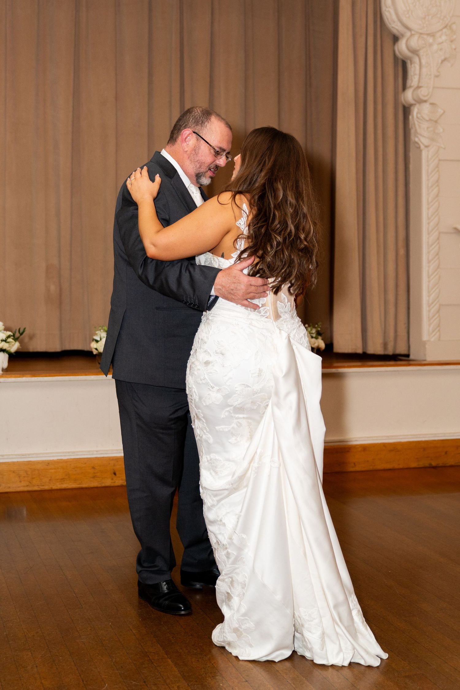 A couple shares their first dance at their wedding reception on a wooden dance floor.