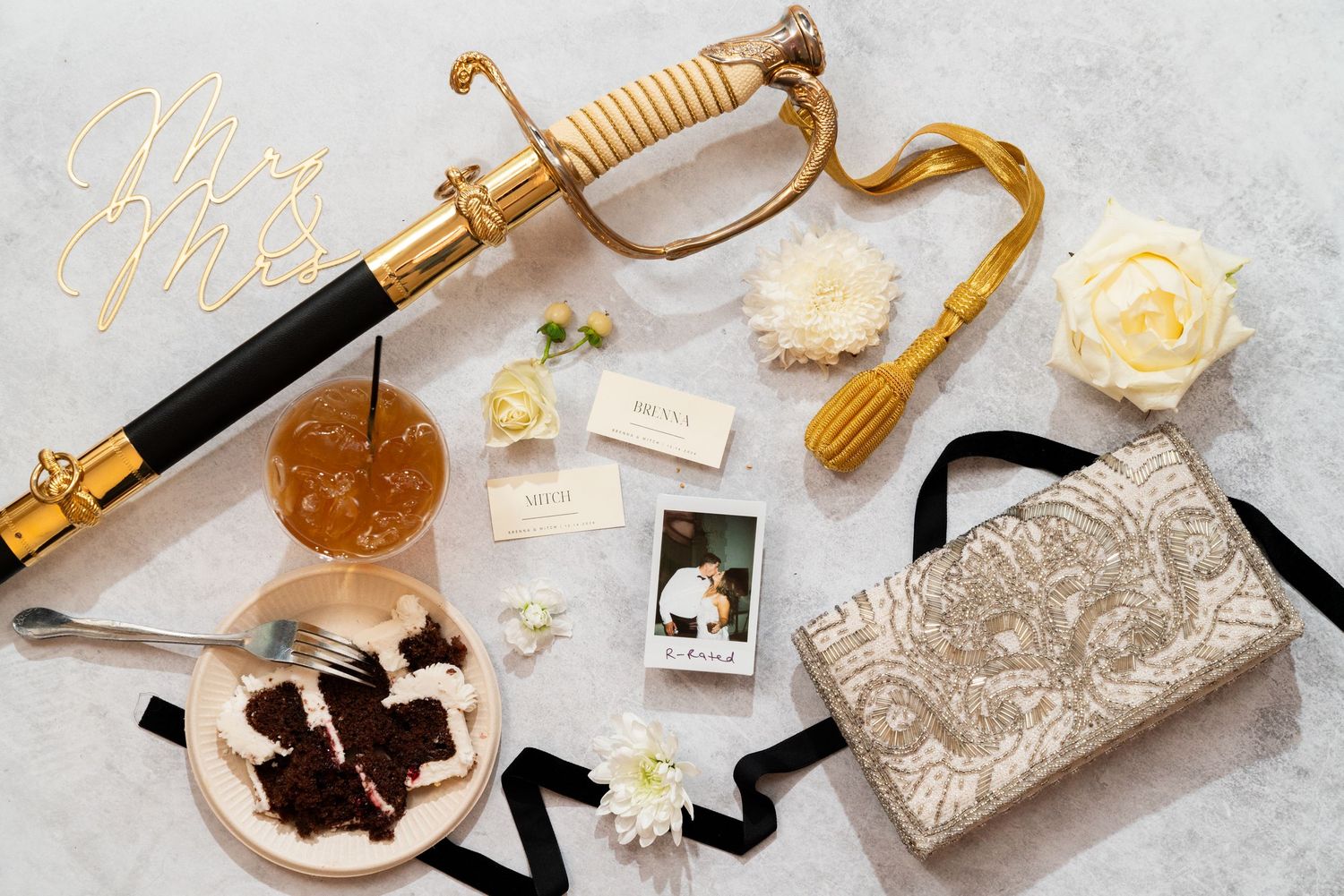 Elegant gold sword decoration with vintage clutch purse, roses, chocolates and black ribbons on marble surface.