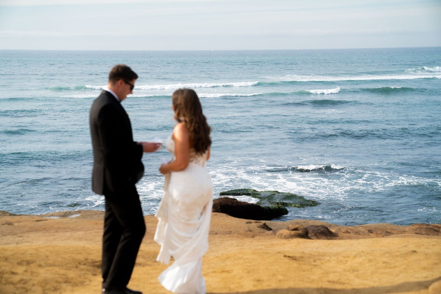 A scenic oceanside wedding moment with waves crashing against rocks in the background.