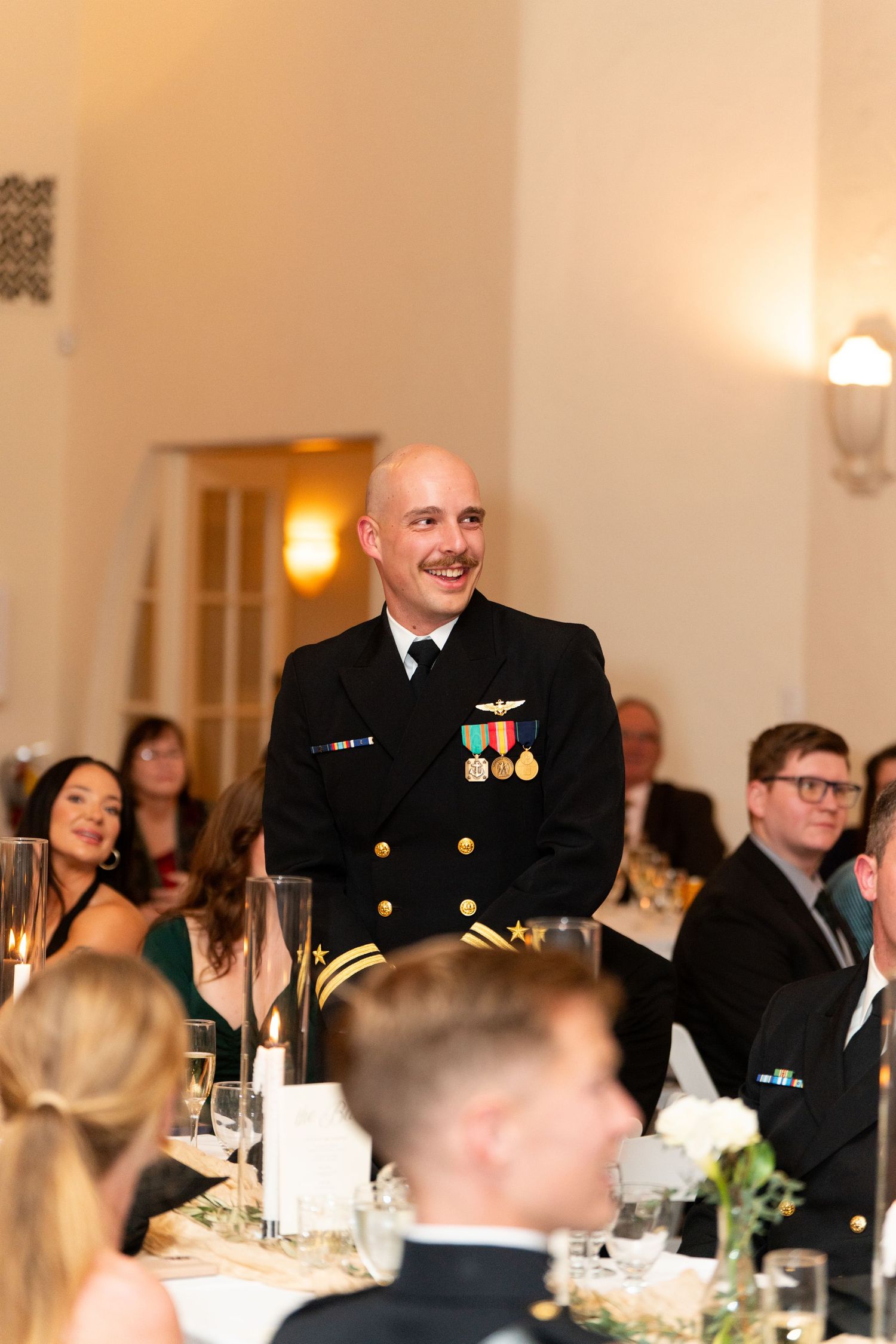 Naval officer in dress uniform giving a speech at elegant wedding reception.