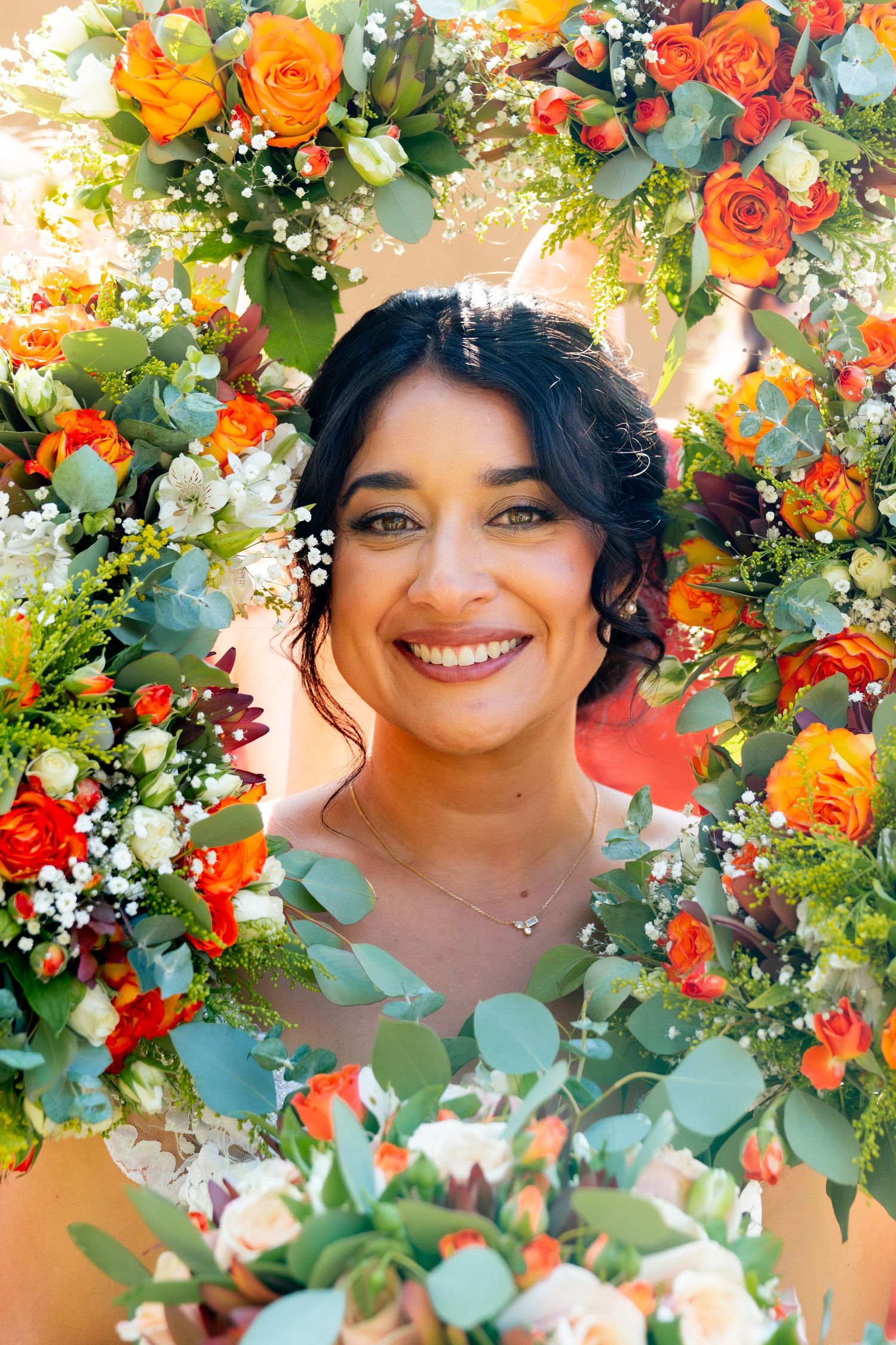 Beautiful floral frame with orange roses, red blooms, and eucalyptus surrounds a joyful celebratory portrait against warm background.