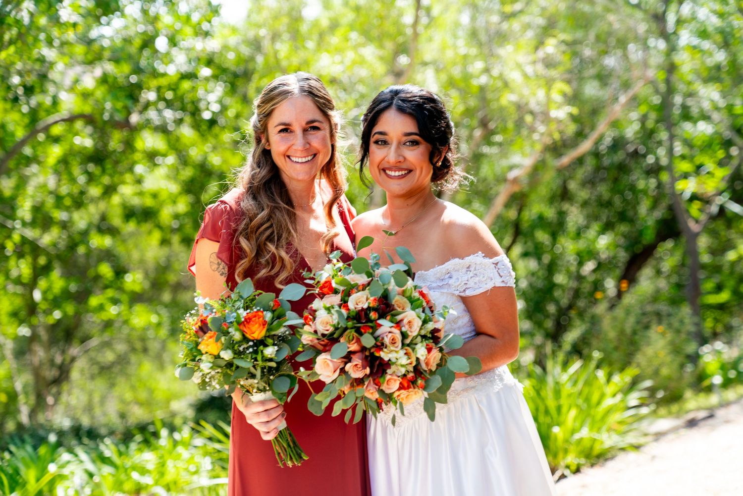 Two people stand together outdoors with lush bouquets featuring bright summer flowers against a green garden background.