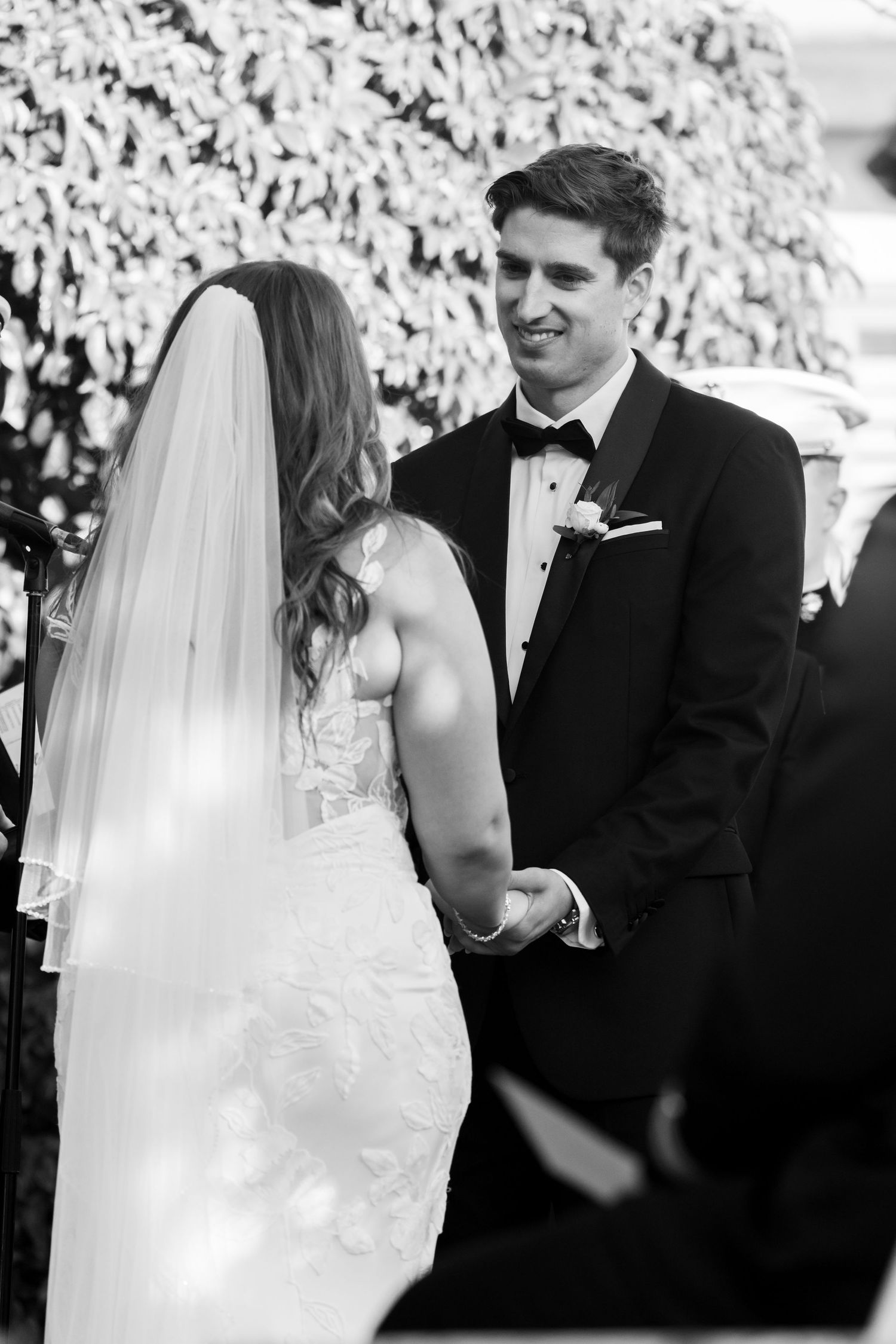 Black and white photo capturing an intimate ceremony moment between newlyweds against a floral backdrop.