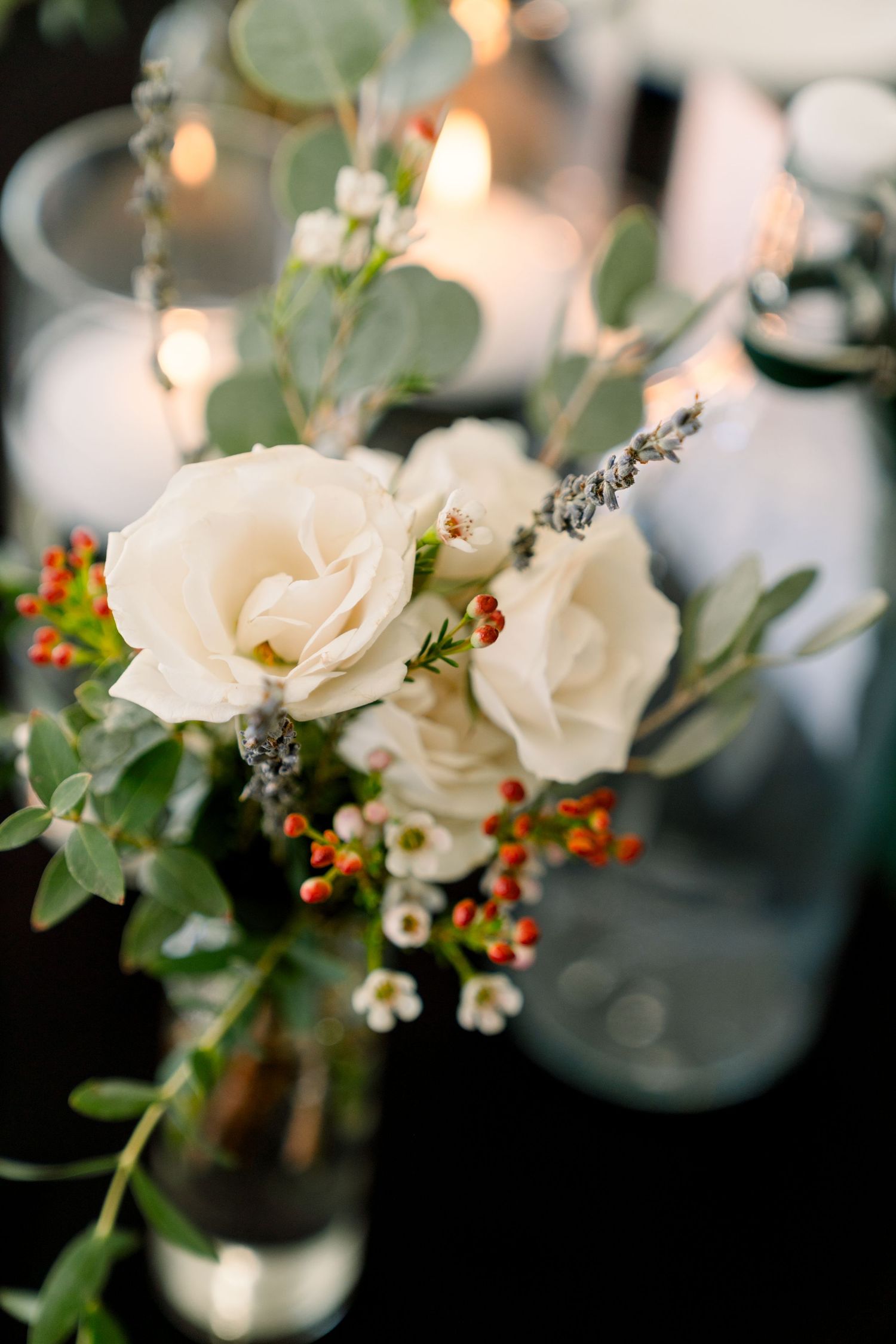 Elegant white roses and greenery floral arrangement in vase with soft bokeh lighting in background.