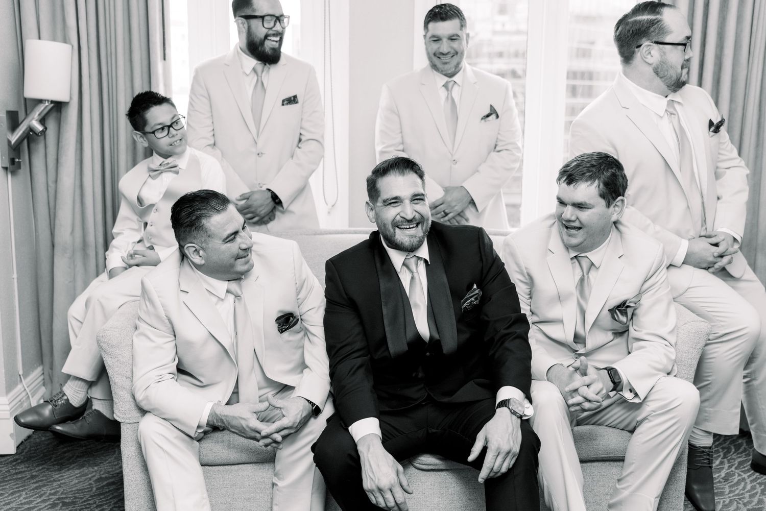 Black and white photograph showing a group wearing white suits sitting and standing together, with one person in dark attire.