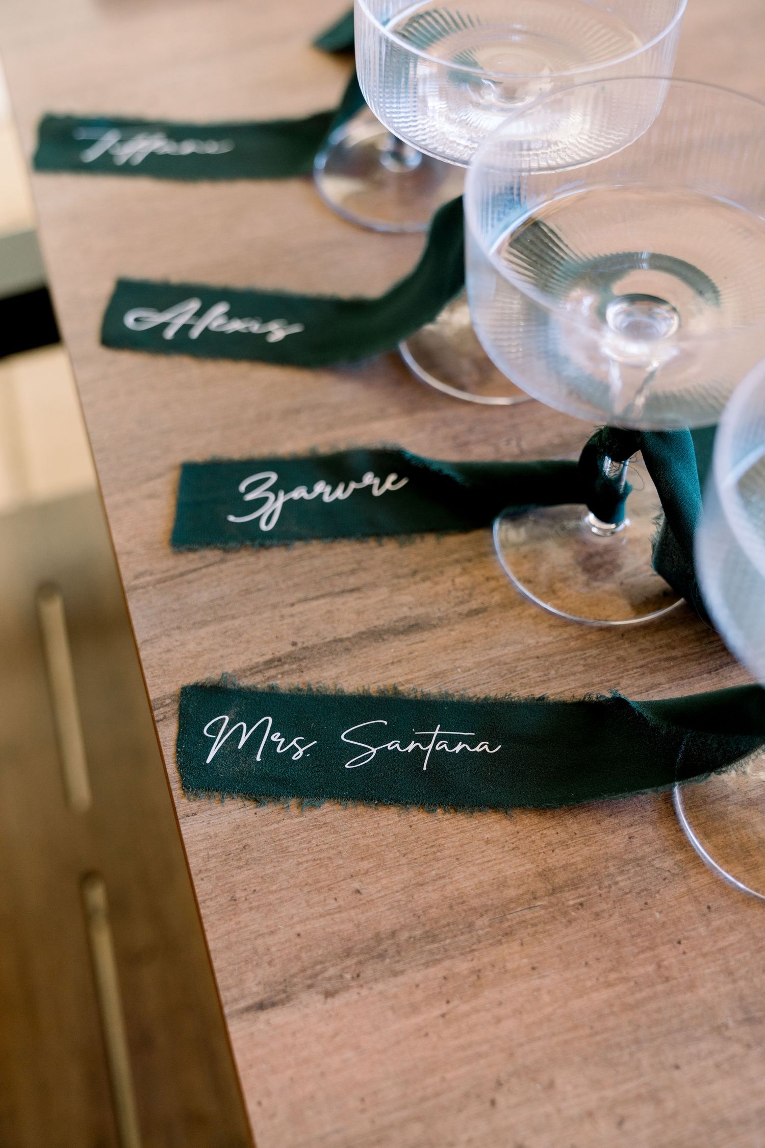Place cards with handwritten names next to wine glasses on a wooden surface.