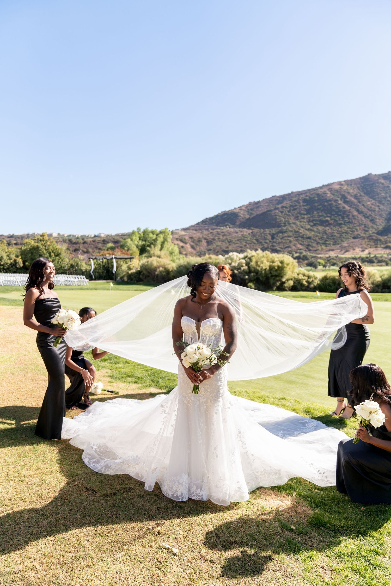 Wedding scene on a golf course with flowing white veil catching the breeze against mountain backdrop.
