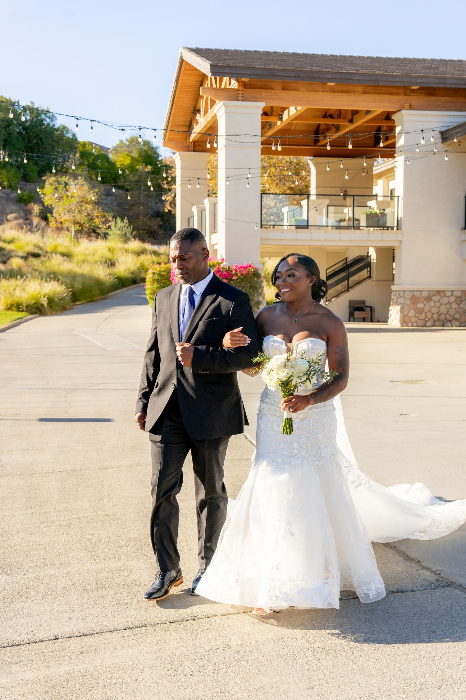 A joyful couple walking together outside a venue with decorative string lights.