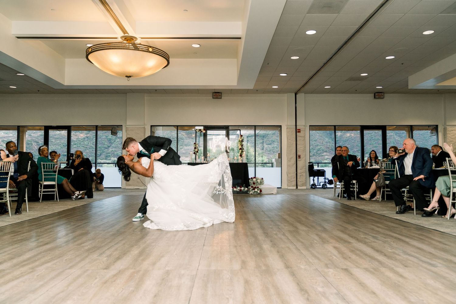 Couple performing first dance in spacious reception hall with natural lighting.