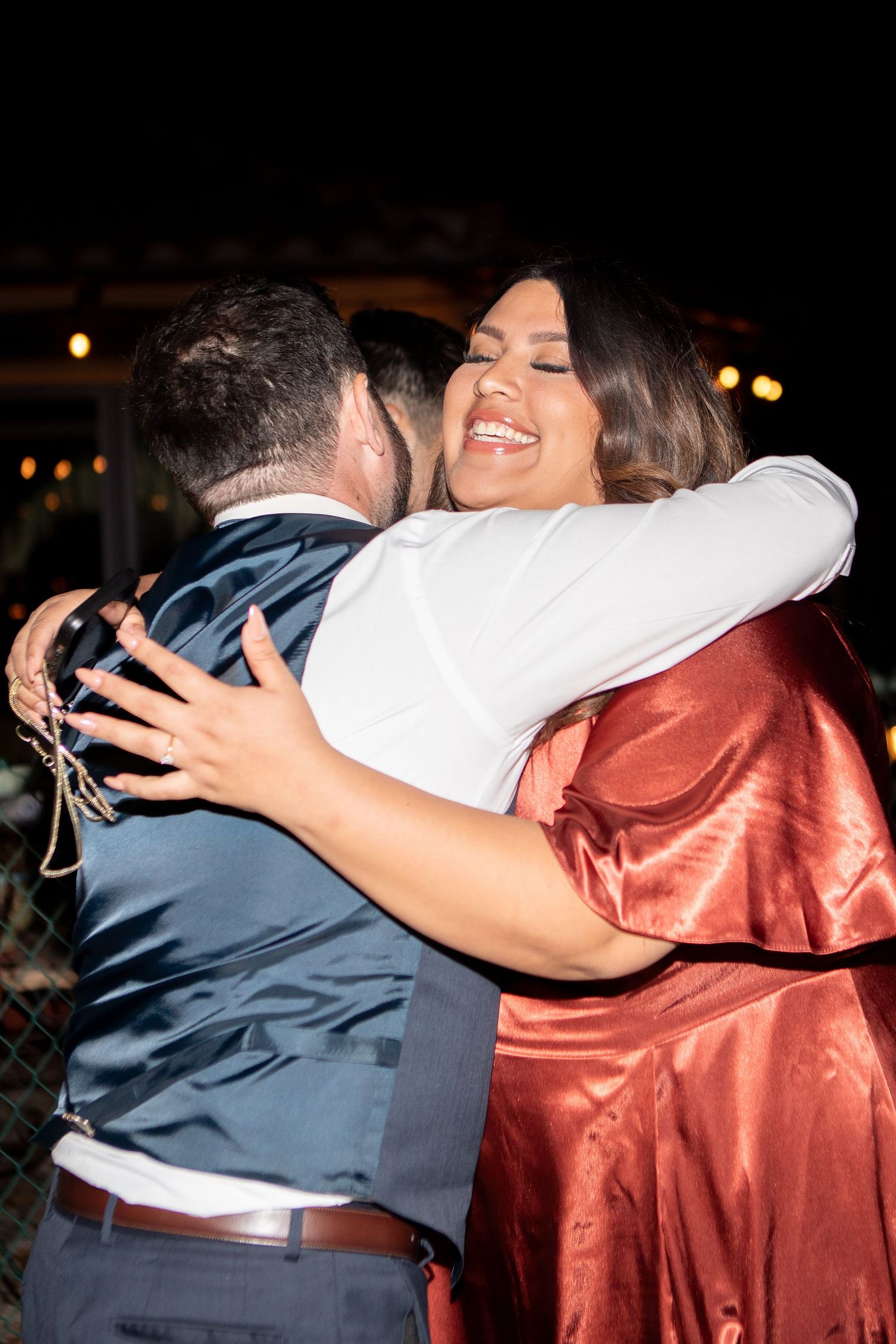 Wedding guests sharing a joyful embrace during evening reception celebration.