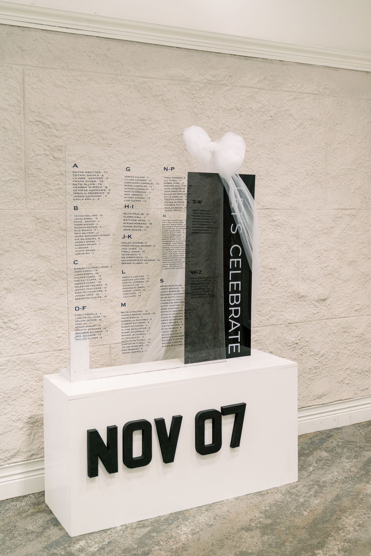 A minimalist white display stand showing 'NOV 07' with a celebration schedule mounted above.