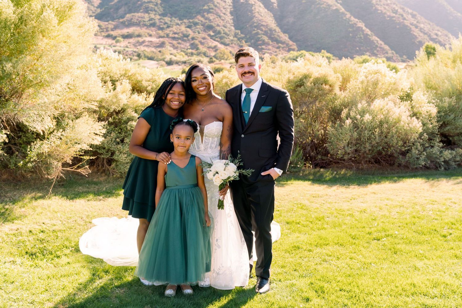 Wedding party poses together outdoors against mountainous backdrop on sunny day in desert landscape.