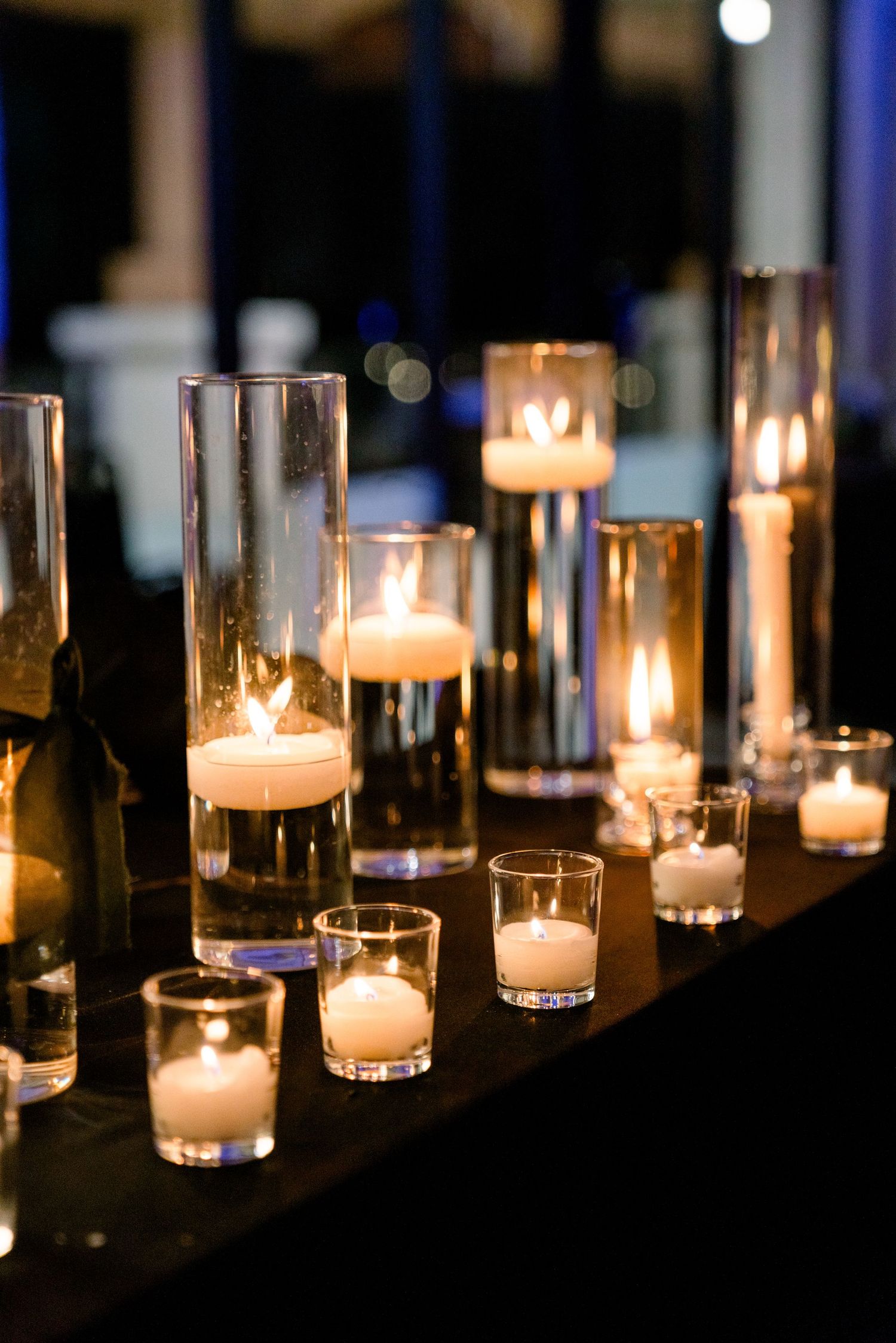 Elegant row of glowing candles in glass cylinders creates romantic ambiance at wedding reception.