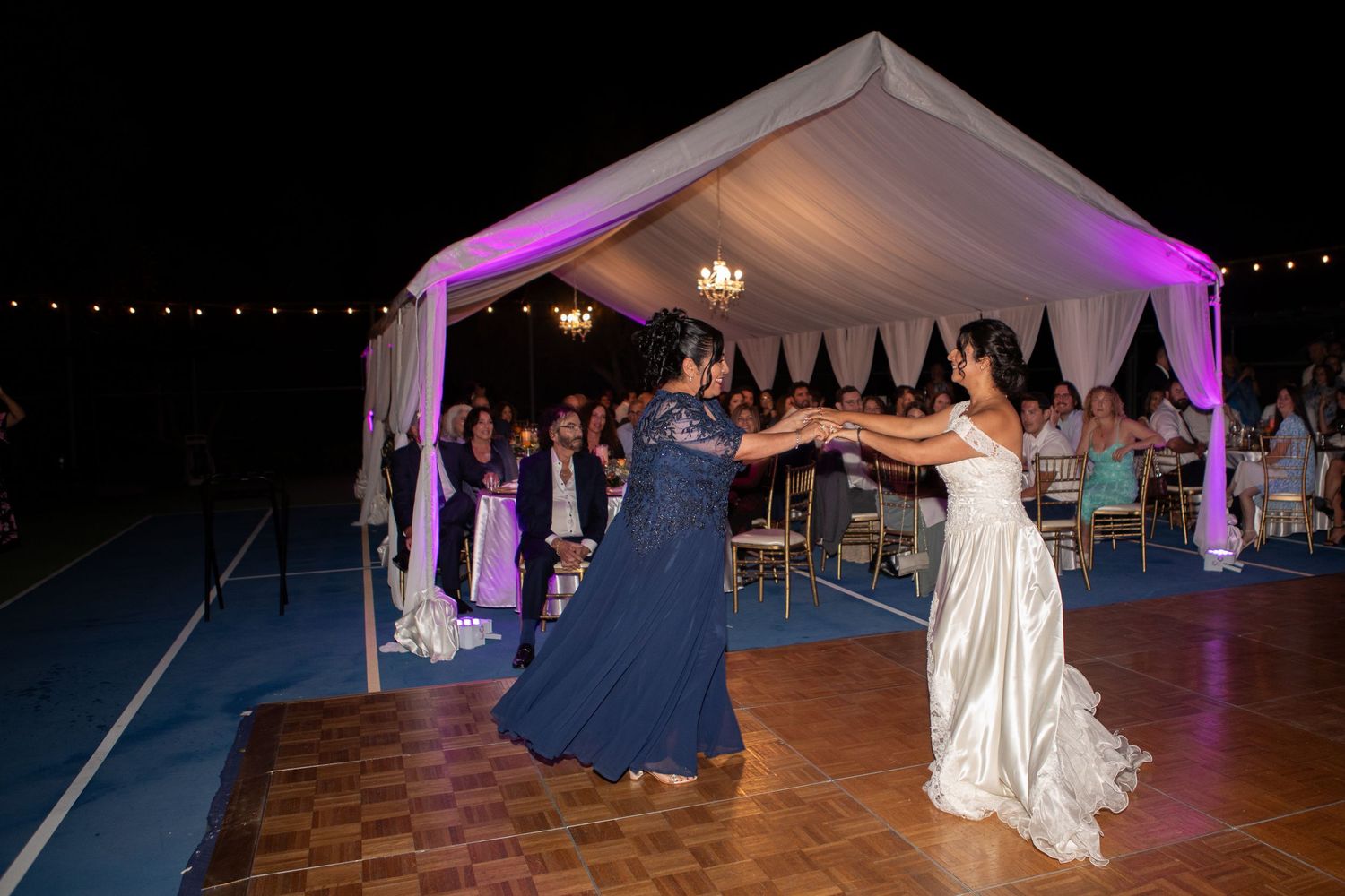 Wedding reception dance under white tent with purple lighting at night.