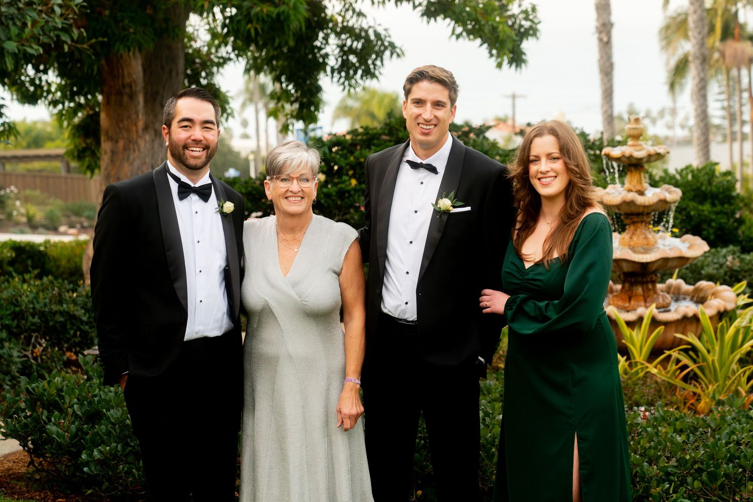 Formal group photo of wedding guests in elegant attire posed in a tropical garden setting.