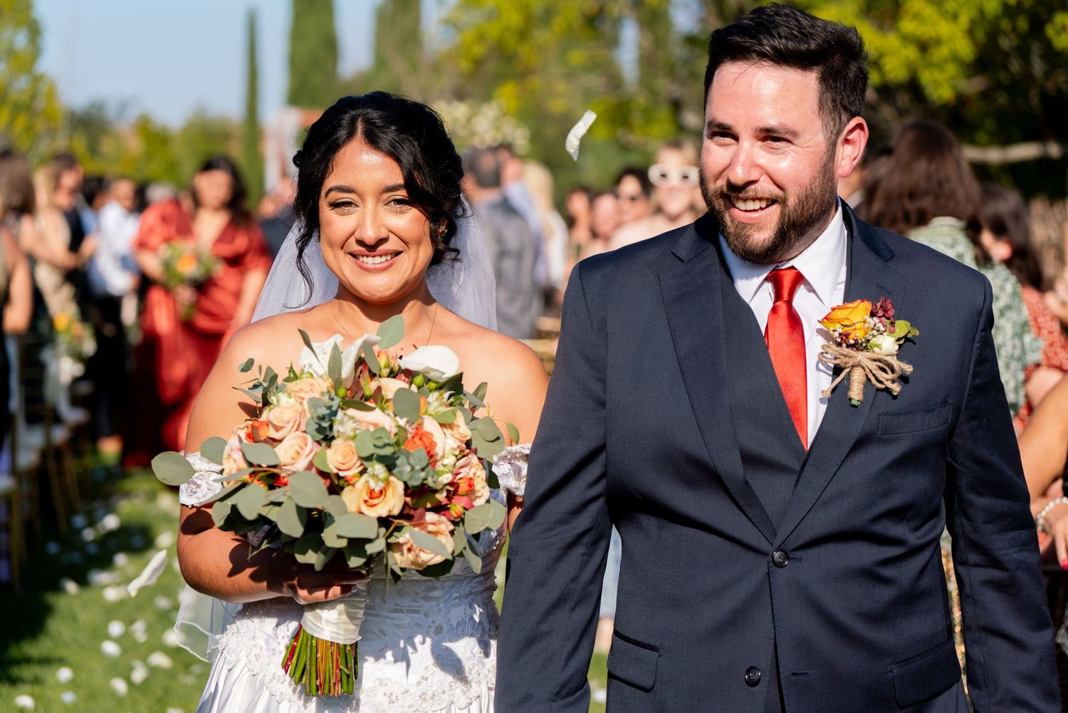 Happy newlyweds celebrate during their outdoor garden wedding ceremony with scattered flower petals.